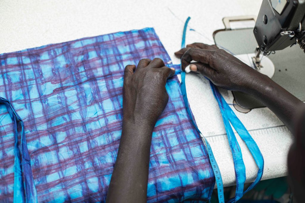 Hands on a sewing machine sewing a blue and purple checked cloth